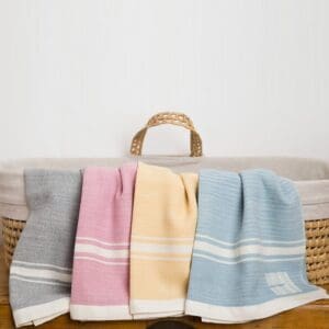 Three pastel-colored towels hanging over a woven basket.