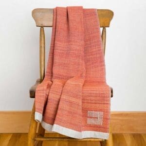 Orange woven blanket draped over a wooden chair with a white label.
