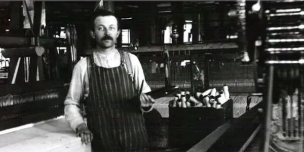 Black-and-white photo of a man in an apron working in a shop.