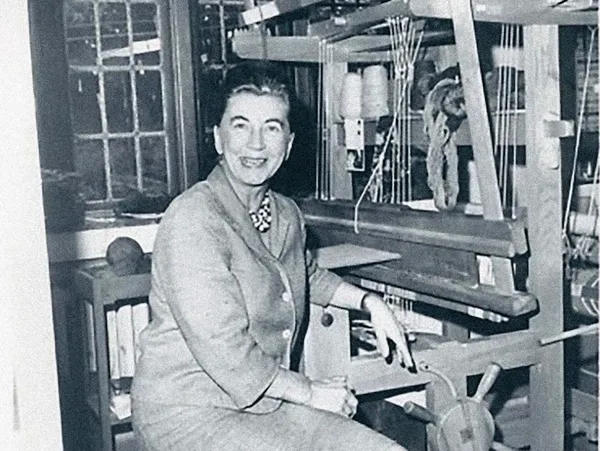A woman sitting beside a loom in a workshop.