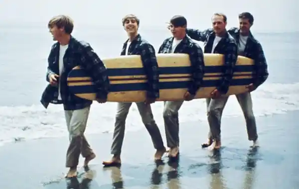 Four men carrying a large wooden boat on a beach.