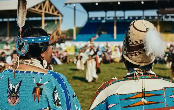 People in traditional Native American attire participate in a cultural outdoor event.