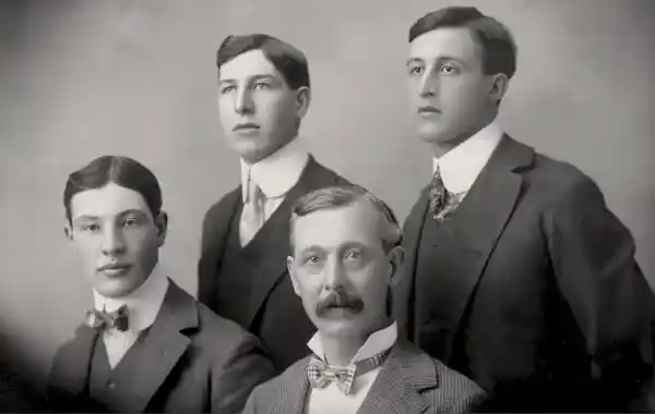 A vintage black-and-white photo of four young men in formal attire.