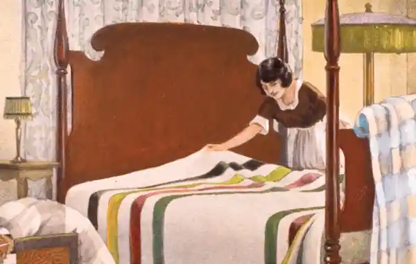 A woman carefully makes a bed with a colorful striped blanket.