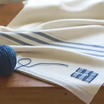 Blue yarn and needle on white cloth with blue stripes.