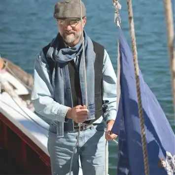 Man in casual clothing stands on a boat near water.