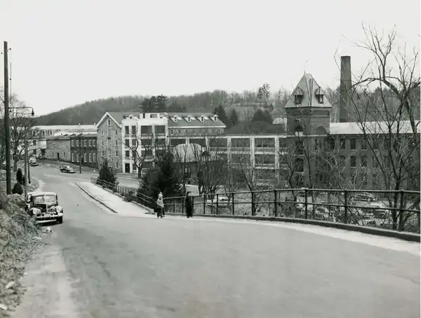 A historic black-and-white photo captures a street leading to an old industrial building.
