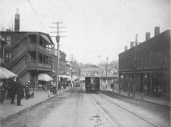 Vintage street scene with trolley and pedestrians in a small town.