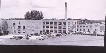 Black and white photo of a large industrial building with many windows and a tall chimney.