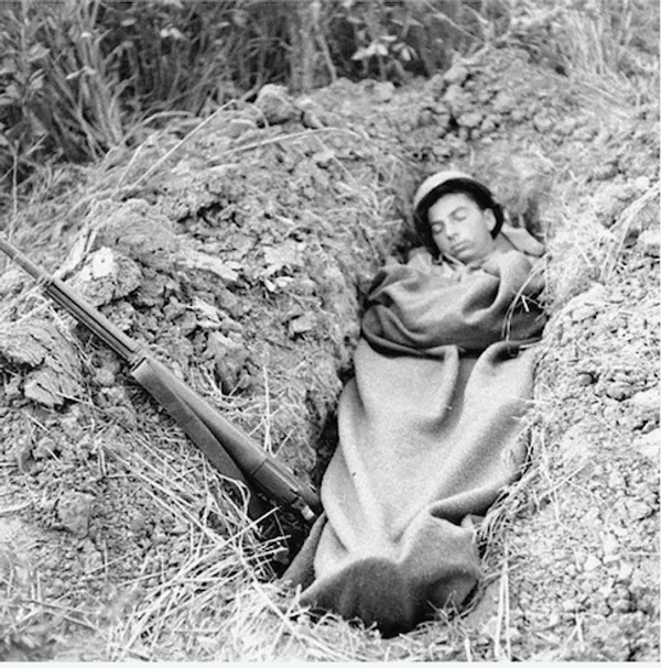 A soldier peacefully sleeping in a shallow trench outdoors.