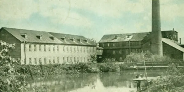 Old black and white photo of two large buildings by a calm water body.