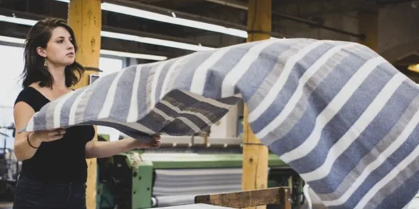 Person weaving large striped fabric on a loom in a workshop.